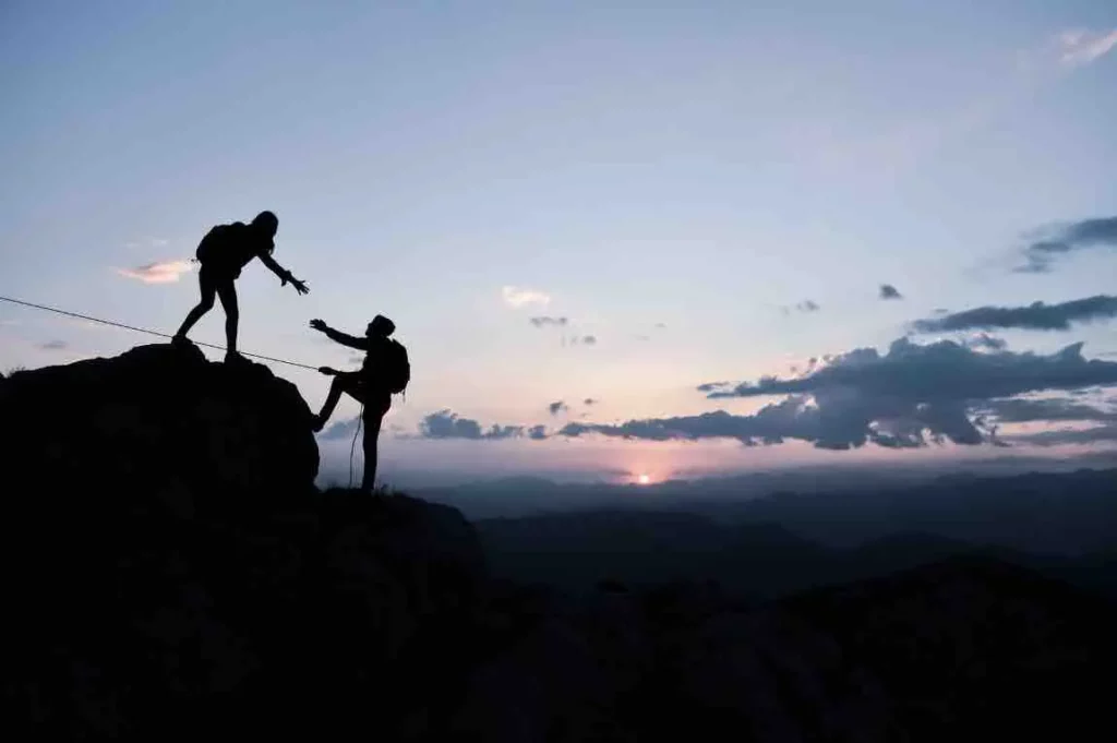 Une personne aide une autre personne a grimper  une montagne