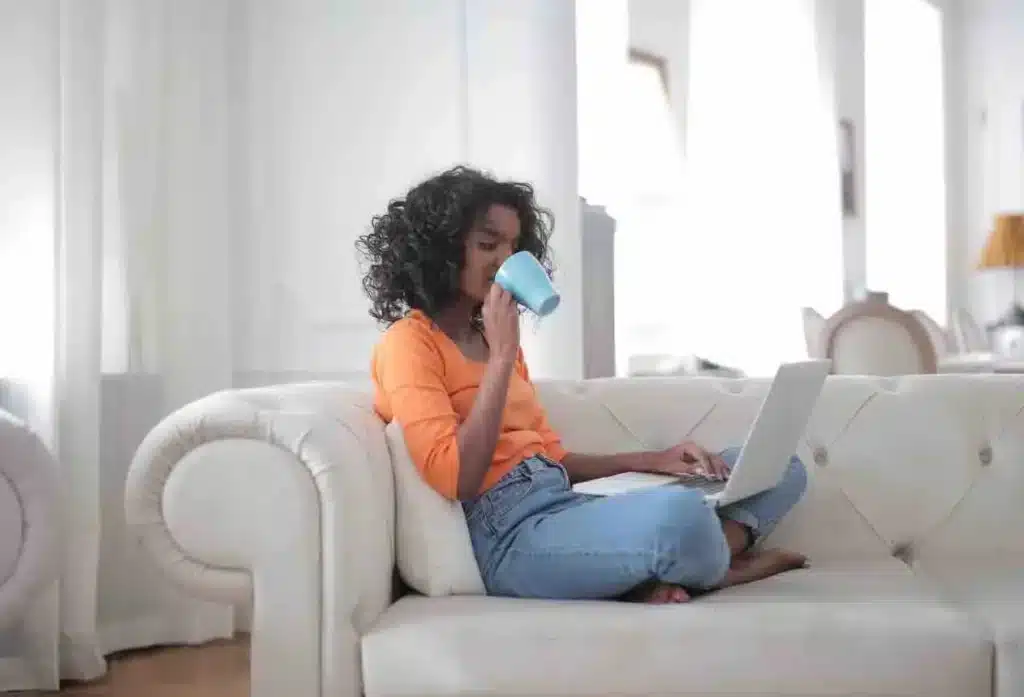 Une femme réalise un bilan de compétences à distance depuis son canapé avec une tasse dans la main