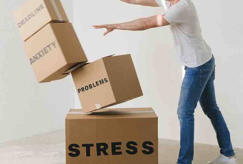 Un homme pousse des cartons où il est écrit "stress" "anxiety" "deadline".