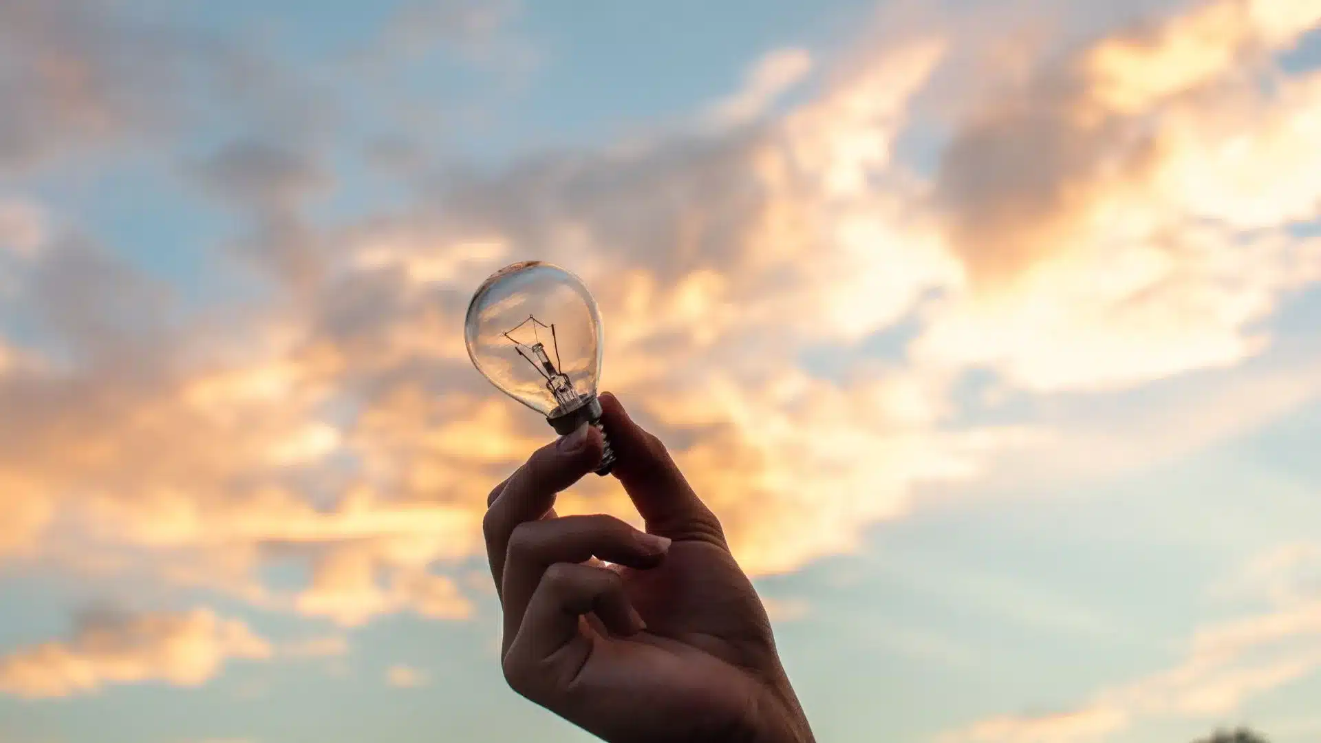 une personne tient une ampoule dans la main et la tend vers le ciel pour représenter l'innovation