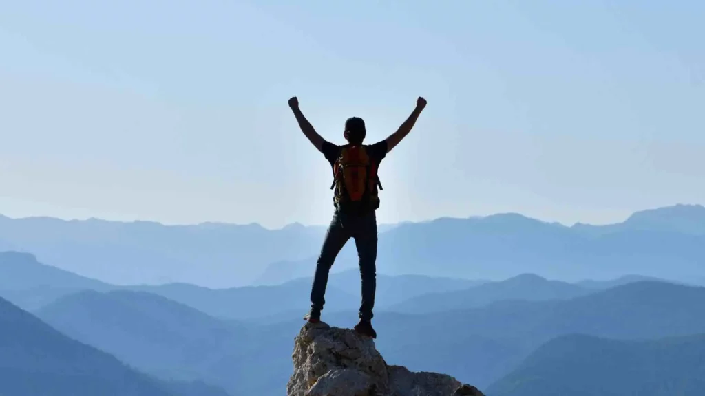 Une personne sur une montagne lève ses mains vers le ciel bleu