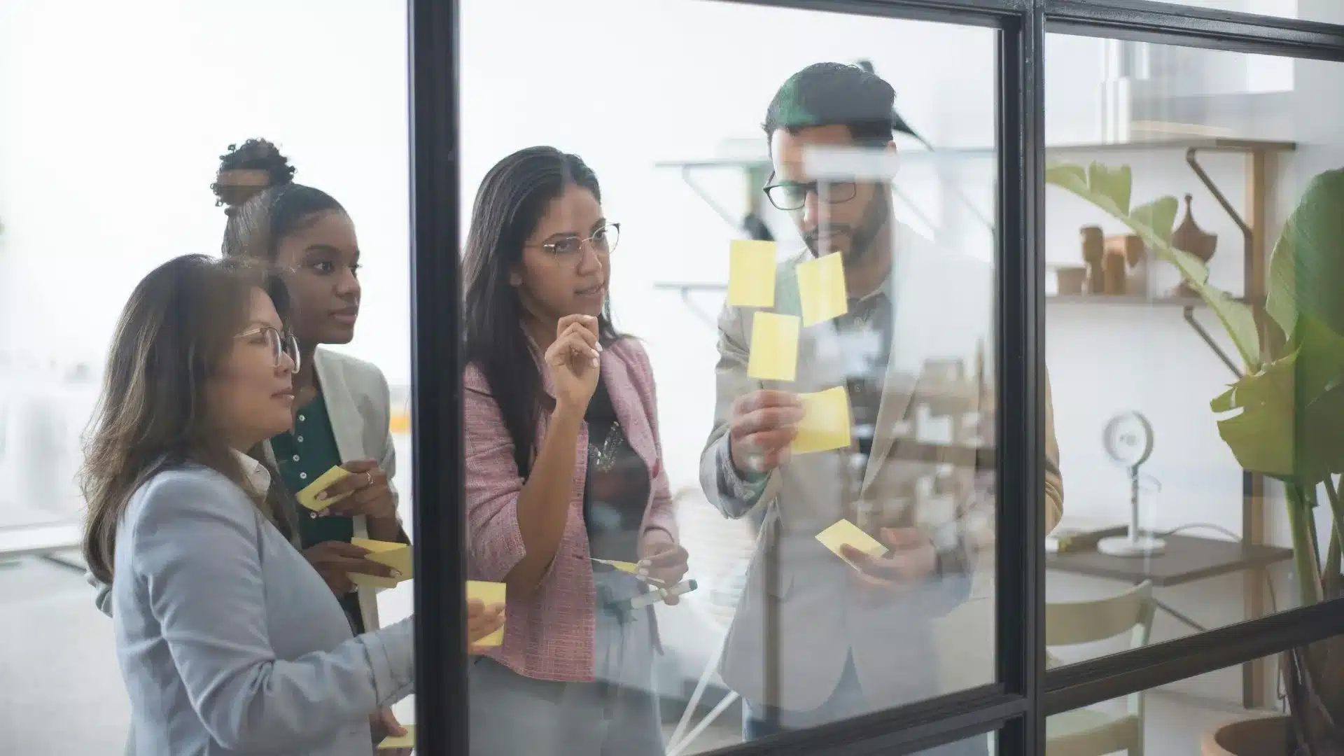 Des personnes en formation professionnelle font un exercice. Quatre personnes sont debout, face à des post-it, en pleine réflexion.