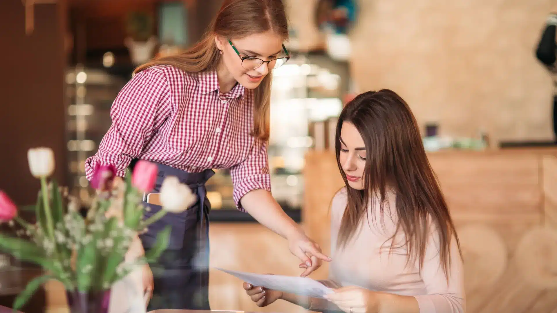 Une femme est assise à une table pour commander à manger. Une autre femme l'aide à choisir à partir du menu.